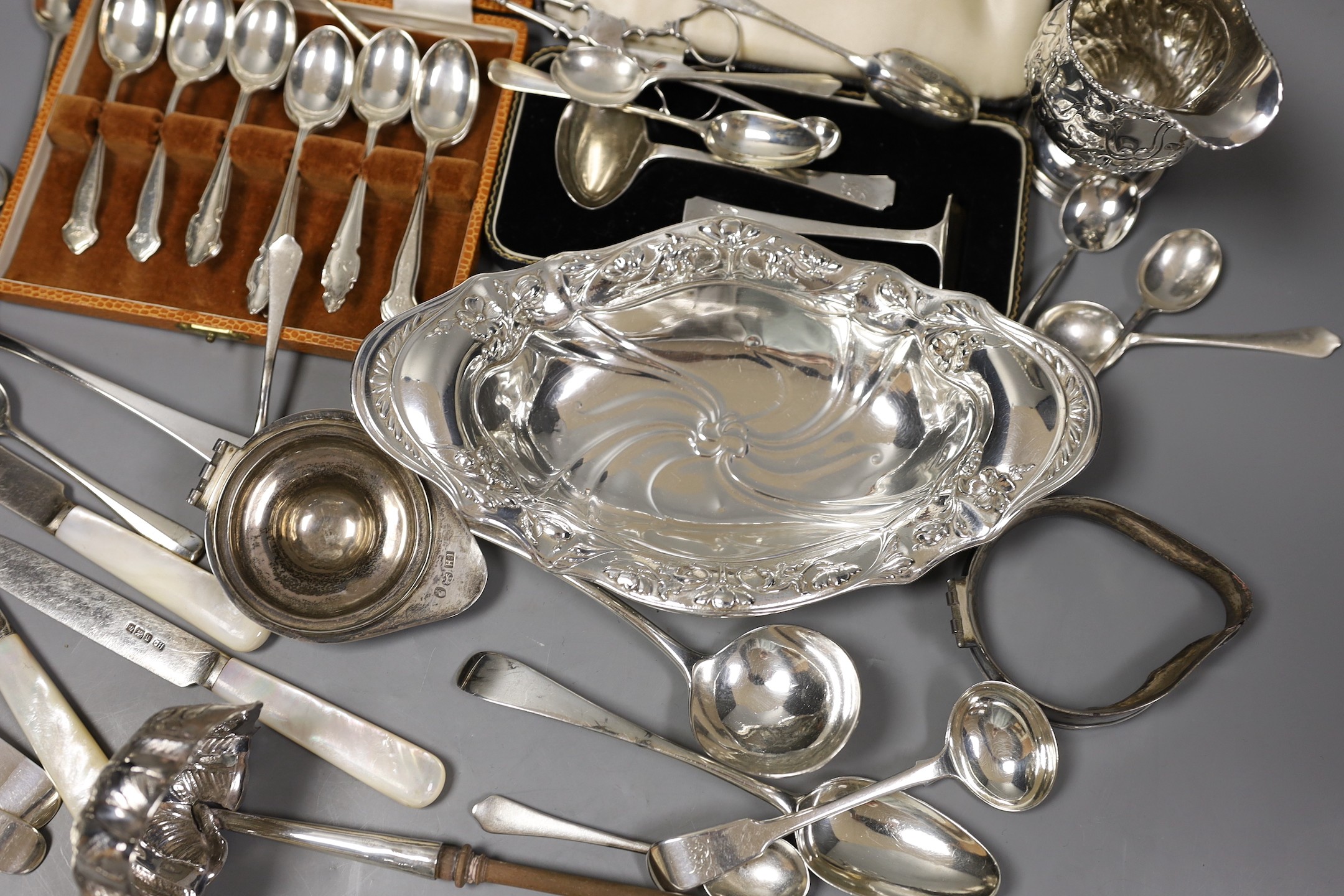 An Edwardian repousse silver oval dish, Birmingham, 1904, 22.8cm, a small quantity of assorted silver flatware including 18th and 19th century pairs of sugar nips, an 18th century silver toddy ladle, white metal cream ju